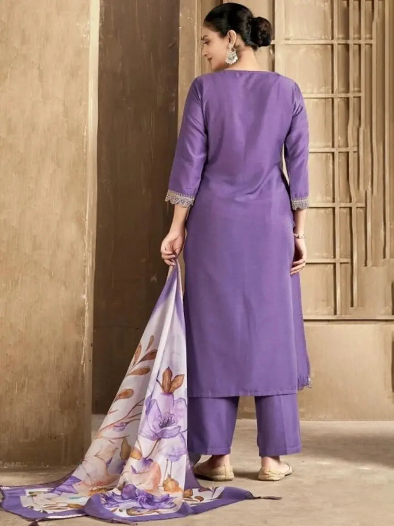 Woman in a purple traditional outfit holding a matching scarf against a beige wall.